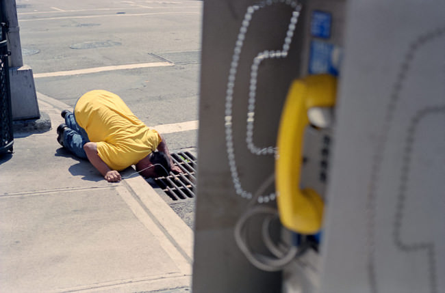 Straßenfotografie von Todd Gross: Ein Mann in gelbem T-Shirt schaut in einen Dohlen