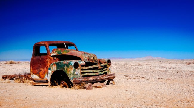 Verrostetes Auto in der Wüste vor blauem Himmel.