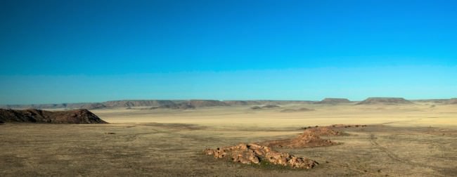Wüstenlandschaft mit einzelnen Plateaus vor blauem Himmel.