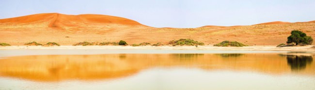 Blick üder die Oberfläche eines Sees vor oranger Dünenlandschaft.