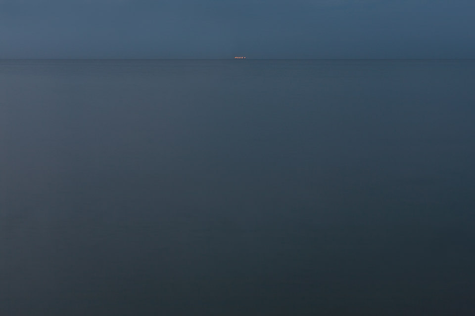 Ein weiter Blick über leeres Meer in der Dämmerung, am Horizont winzige Lichter.