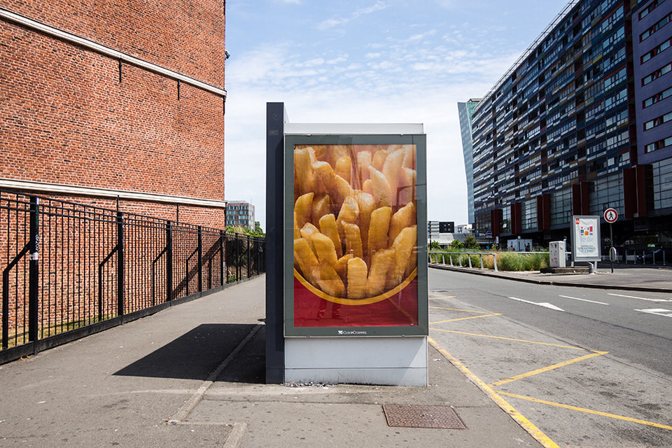 Blick auf eine leere Straße, die von einem großen Plakat mit Pommes Frites geschmückt ist. 