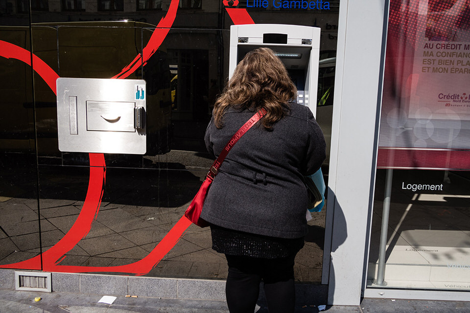Eine Frau mit roter Tasche steht an einem Geldautomat. 