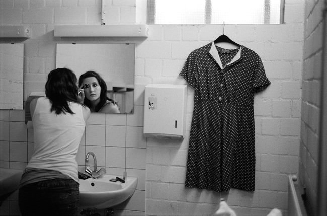 Eine Frau vor einem Spiegel, ein Kleid an der Wand.