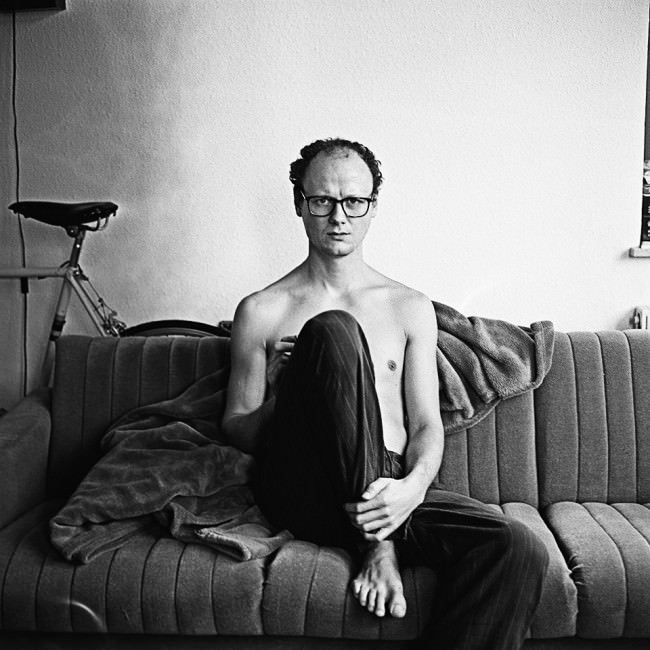Ein Mann mit Brille sitzt auf einer Couch.