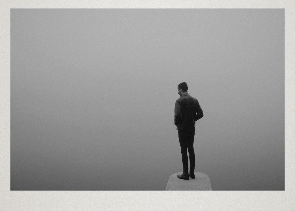 Eine Person steht am Ende eines Steges im Nebel.