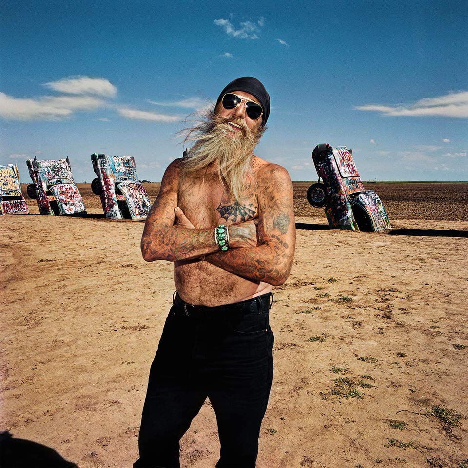 Mann mit langem Bart und Tattoos vor der Cadillac Ranch.