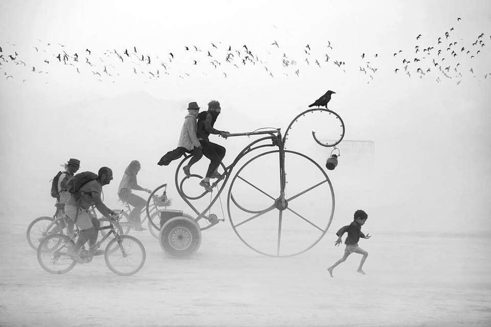 Ein seltsamen Gefährt gefolgt von drei Fahrrädern und einem kleinen Jungen in der Wüste.