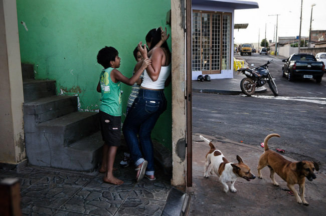 Zwei Jungs bedrängen eine Frau in einem Treppenhaus, daneben laufen draußen zwei Hunde um die Straßenecke.