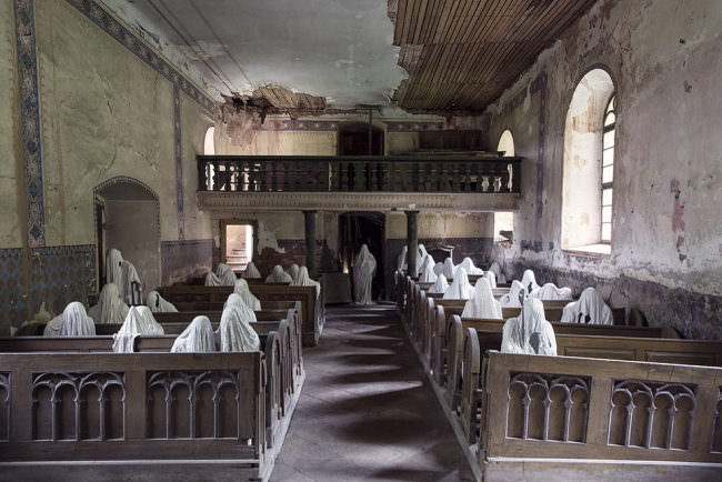 Über 30 Geister aus Gips in einer Kirche sitzend.