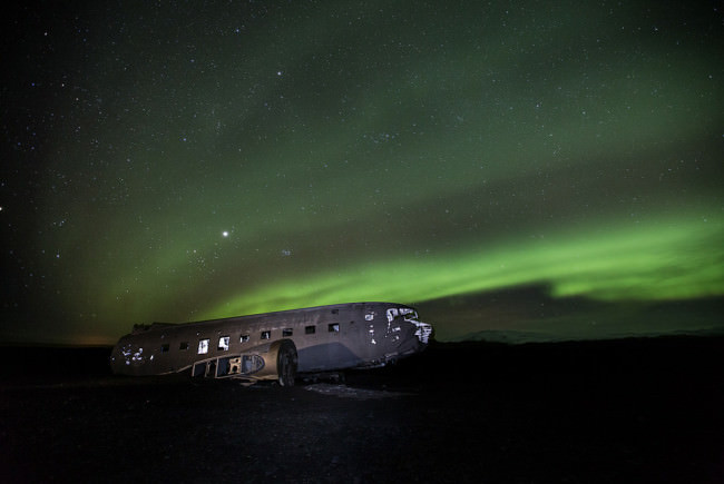 Flugzeugwrack bei Nacht. Polarlichter im Hintergrund.