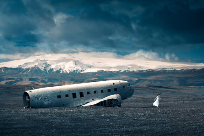 Eine Frau im weißen kleid läuft von einem Flugzeugwrack weg.