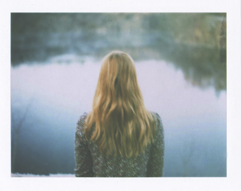 Eine Frau steht mit dem Rücken zur Kamera und sieht in ein Gewässer.