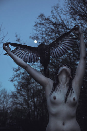Eine nackte Frau hält einen toten Vogel mit ausgebreiteten Flügeln über sich.