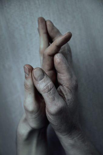 Zwei Hände mit fehlendem Finger berühren sich.