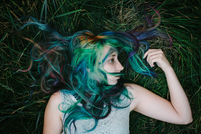 Eine Frau mit bunten Haaren im Gras liegend.
