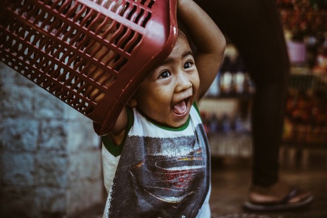 Ein Kind spielt mit einem roten Plastikkorb und freut sich.
