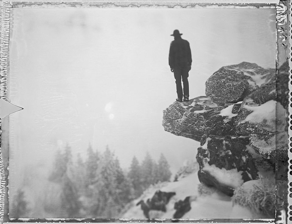 Ein Mann steht auf einer Felsenklippe und sieht in die eisige Landschaft.