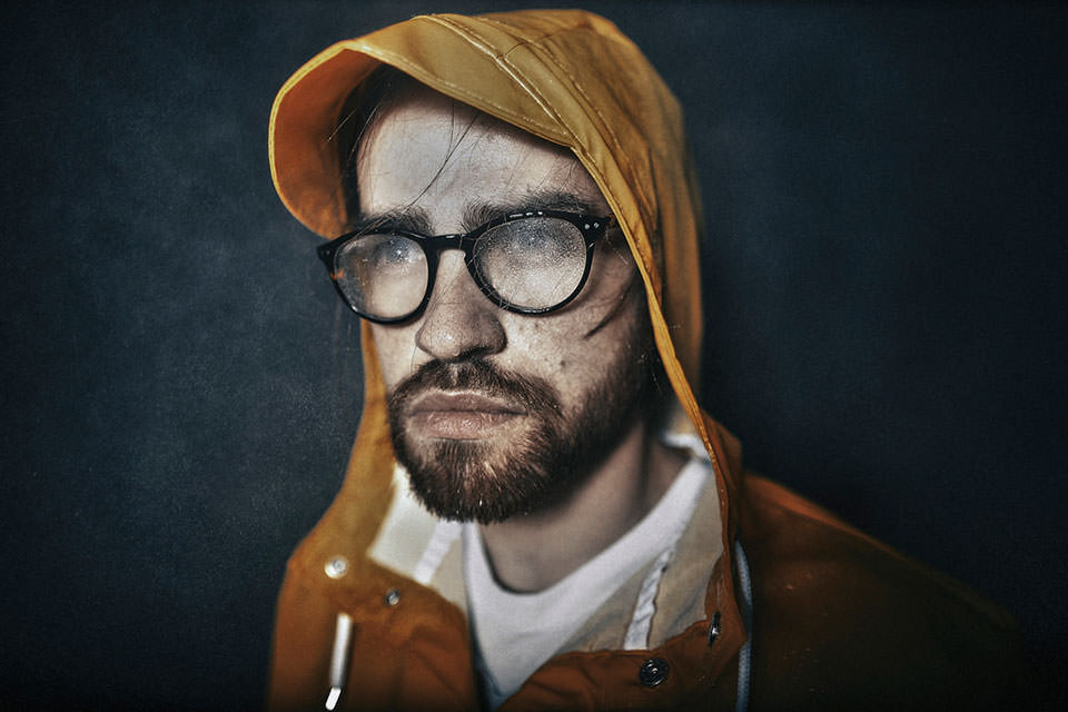 Portrait eines Mannes mit Regenjacke und Regenspritzern auf der Brille.