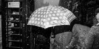 Eine Straßenfotografie mit einem Schirmträger, es schneit.