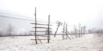Gatterartige Holzkonstruktionen und ein schiefer Telegrafenmast in einer Schneelandschaft.