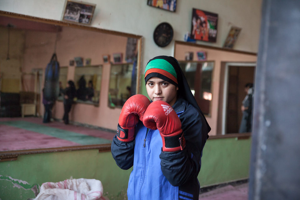 Eine junge Frau mit Kopftuch trägt Boxhandschuhe und hält diese in Pose zur Kamera.