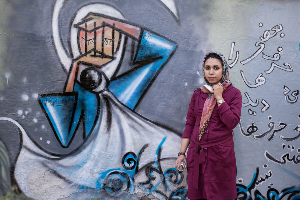 Eine Frau posiert vor einer Graffittiwand.