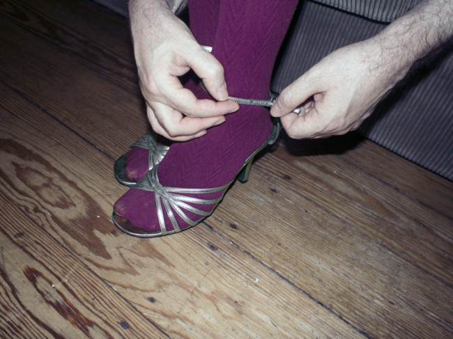 Männerhände schließen silberne Stilettos Füßen in purpurner Strumpfhose.