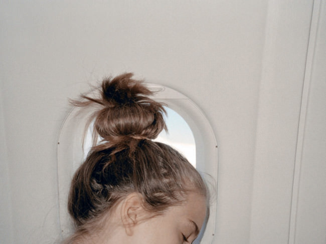 Ein Frauenkopf mit lustigem Zopf lehnt schlafend an einem Flugzeugfenster.