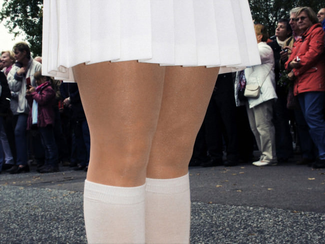 Frauenbeine, eingefasst von einem weißen Faltenrock und weißen Kniestrümpfen.
