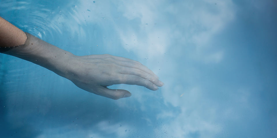 Eine Hand greift ins Wasser, indem sich die Wolken spiegeln.