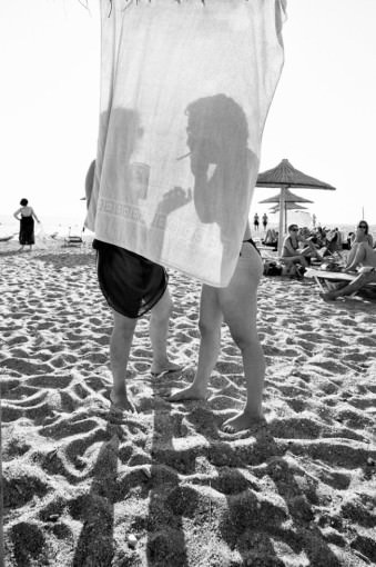 Zwei Frauen stehen am Strand hinter einem Handtuch.