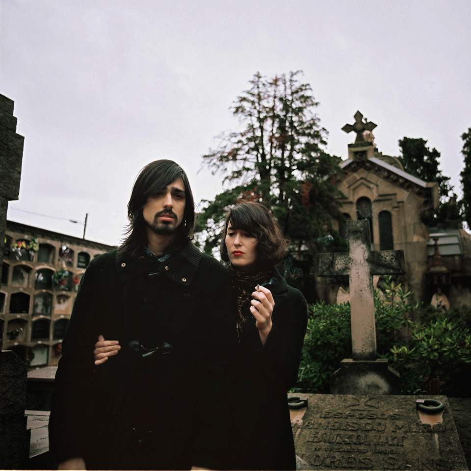 Ein Paar in schwarzer Kleidung auf einem Friedhof.
