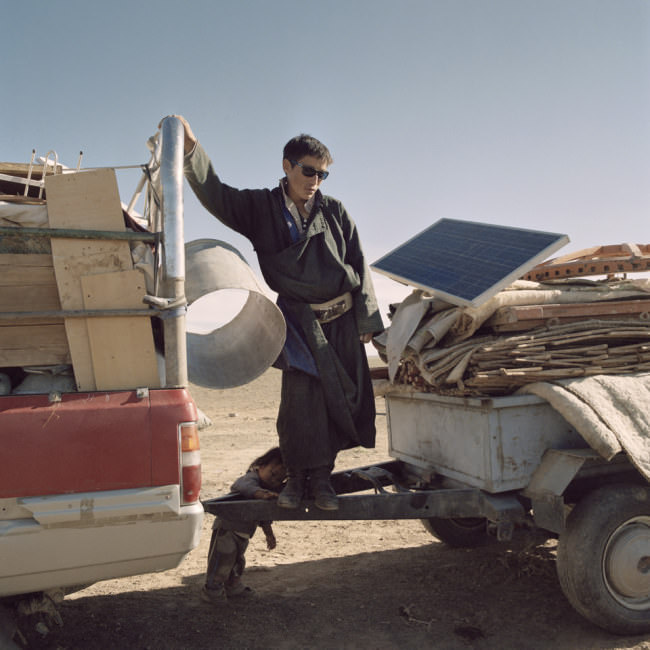 Ein Mann steht auf einem voll beladenen Lastzug mit den Habseligkeiten der Nomdenfamilie.