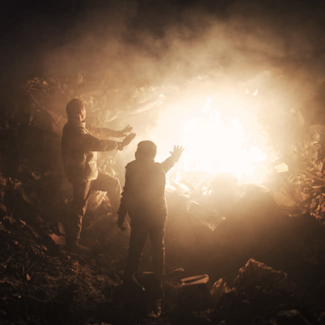 Zwei Männer stehen an einem Feuer auf einer Mülldeponie, wo sie nach Wiederverwendbarem suchen.