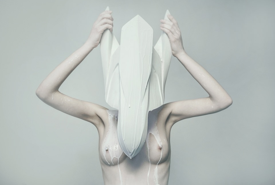 Portrait einer nackten Frau mit weißer Skulptur über den Kopf gestülpt, aus der eine weiße Flüssigkeit fließt.