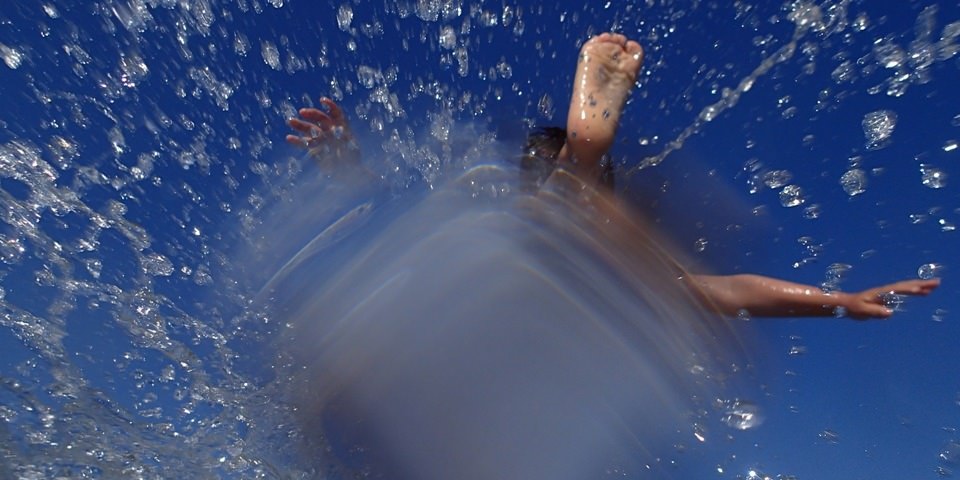 Füße und eine Hand in einer Wasserfontäne vor blauem Himmel.