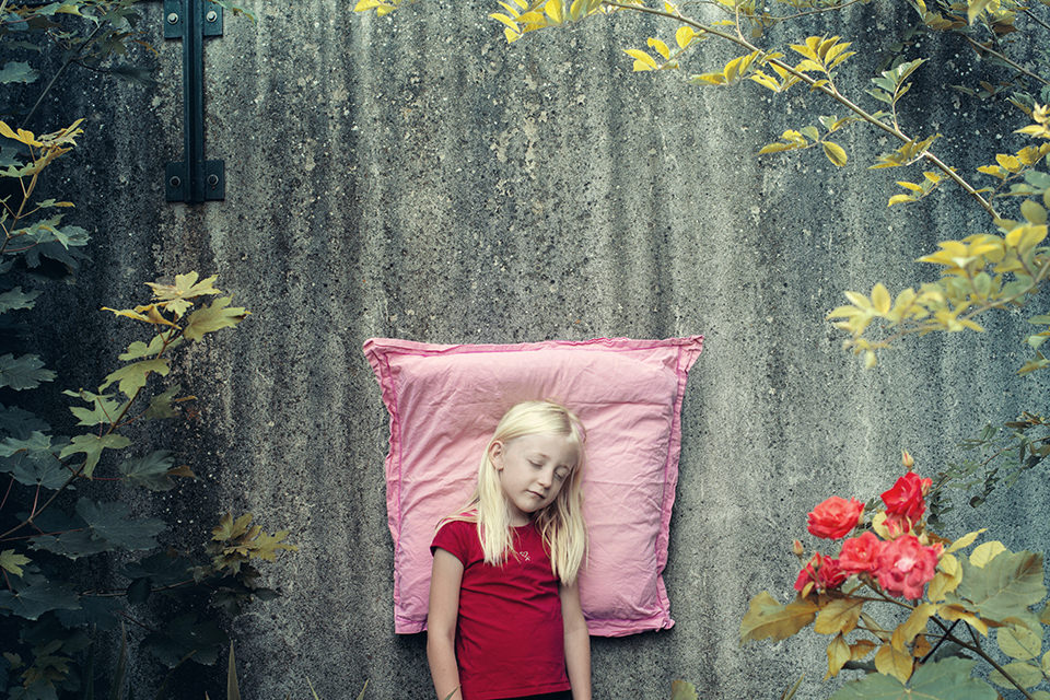 Ein auf einem rosa Kissen schlafendes Mädchen lehnt an einer Wand.