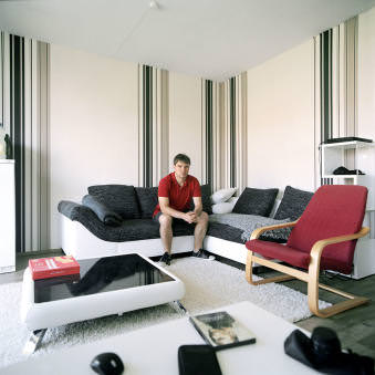 Ein junger Mann sitzt auf dem Sofa in seinem Wohnzimmer