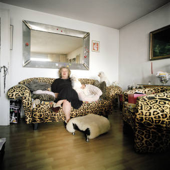 Eine ältere Dame mit ihren zwei Schoßhündchen auf einem Sofa mit Leopardenmuster