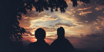 Zwei Personen schauen sich einen malerischen Sonnenuntergang an.