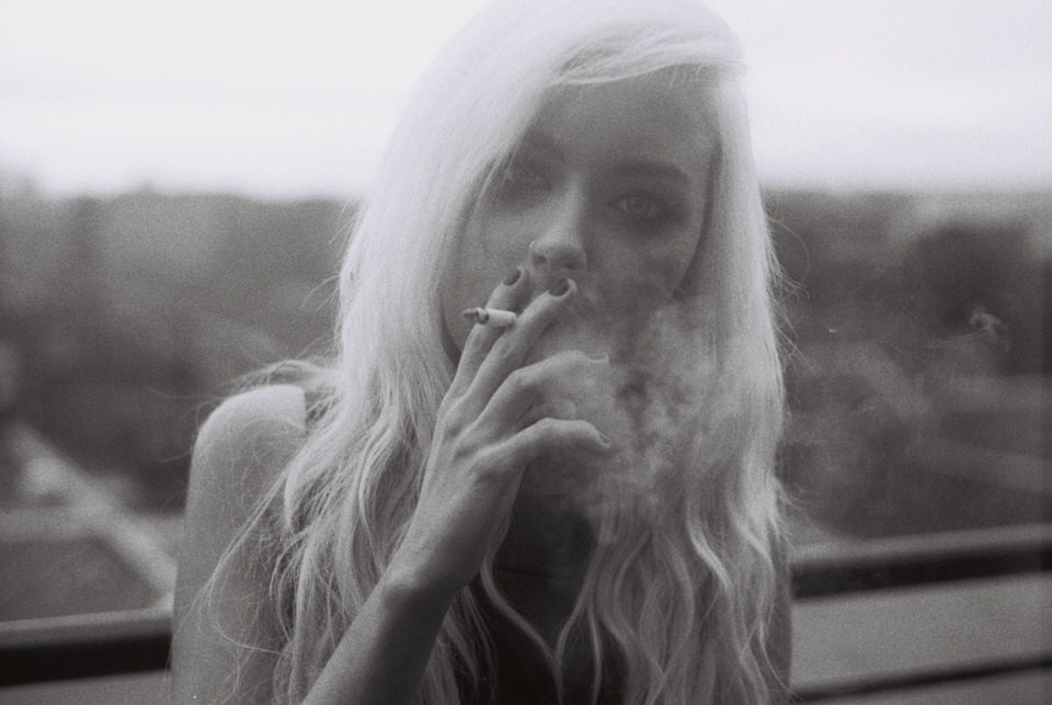 Eine Frau raucht eine Zigarette und schaut in die Kamera. 