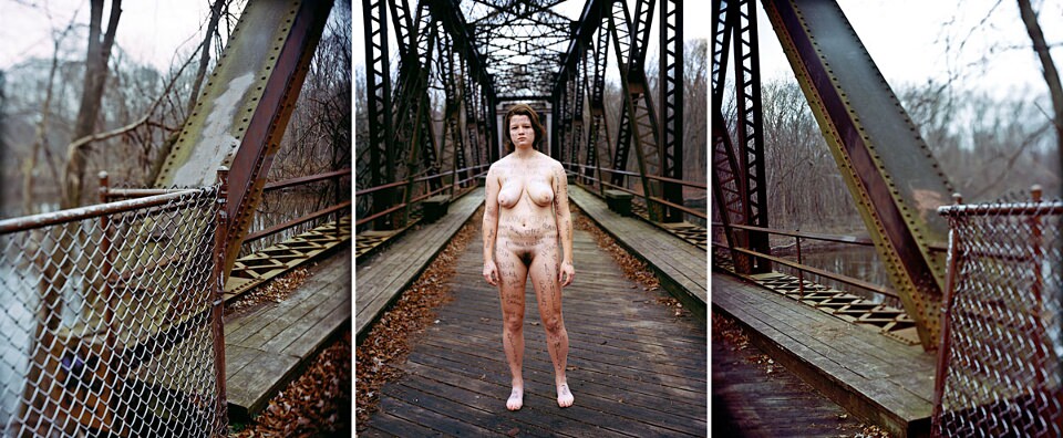 Eine nackte und beschriftete Frau steht auf einer Brücke.