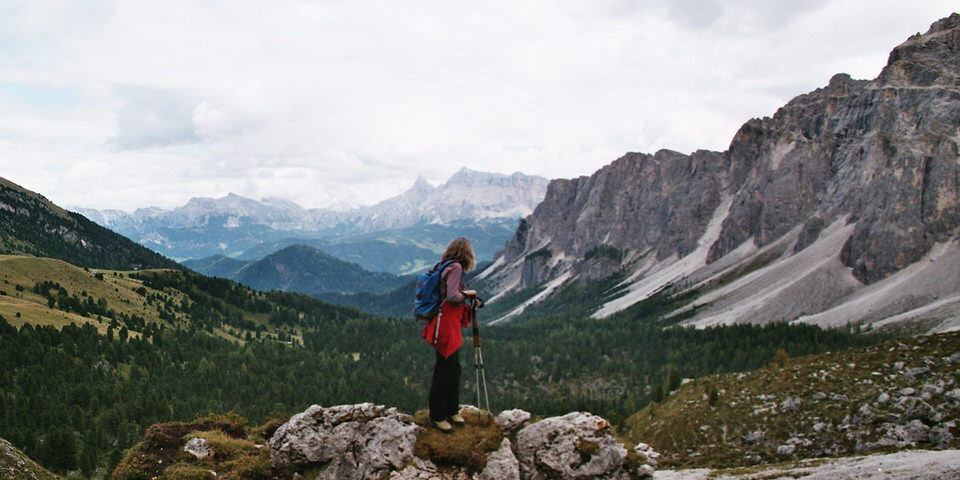 Wanderin auf einem Hügel blickt in die Alpenlandschaft.