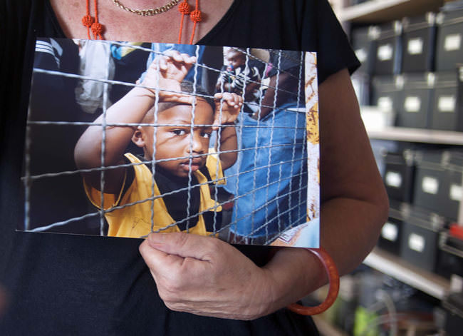 Ein dunkelhäutiger Junge steht in der Anlufstelle für Asylsuchende an einem Zaun und schaut verlegen in die Kamera.