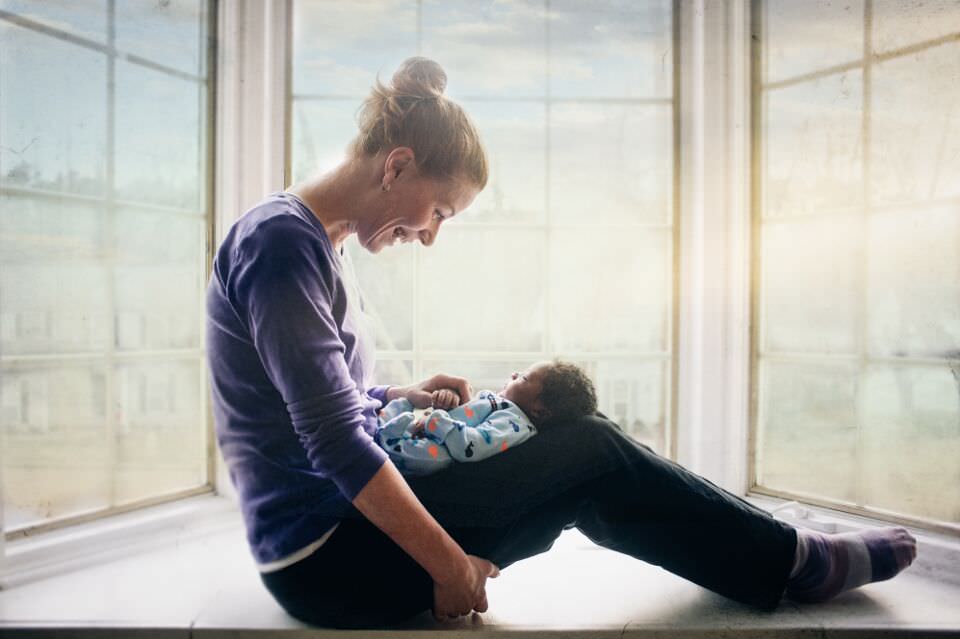 Eine Mutter sitzt im Fenster und schaut ihr Kind an.