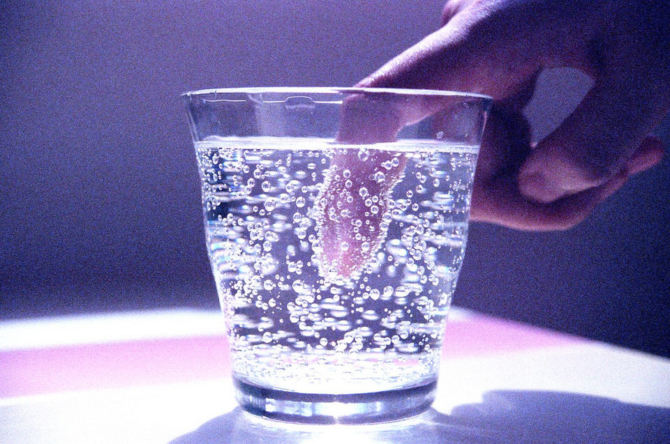 Ein Finger wird in ein Glas Sprudel eingetaucht. 