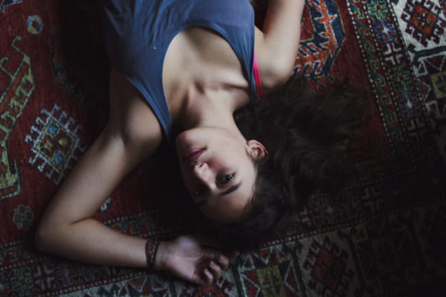 Junge Frau liegt auf einem Teppich und blickt in die Kamera.