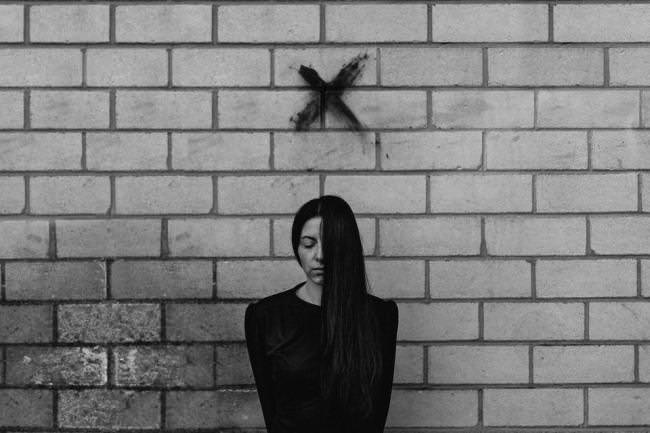 Frau an einer Mauer mit schwarzem X über dem Kopf.