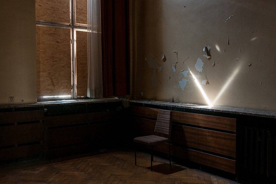 Ein Lichtstrahl fällt in einen verbarrikadierten Raum und spiegelt sich auf einer Platte an der Wand.